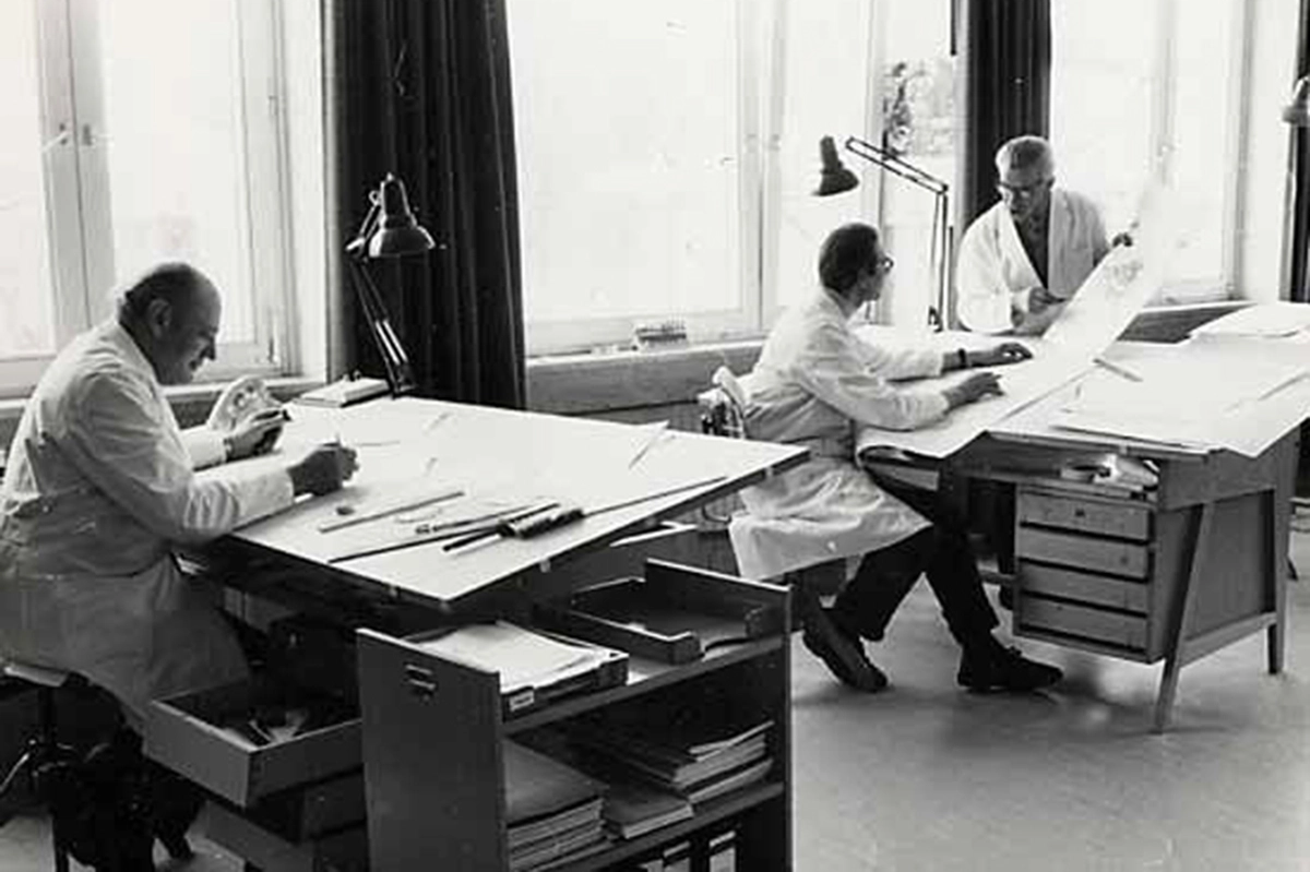 Two desks, three men working on paper 