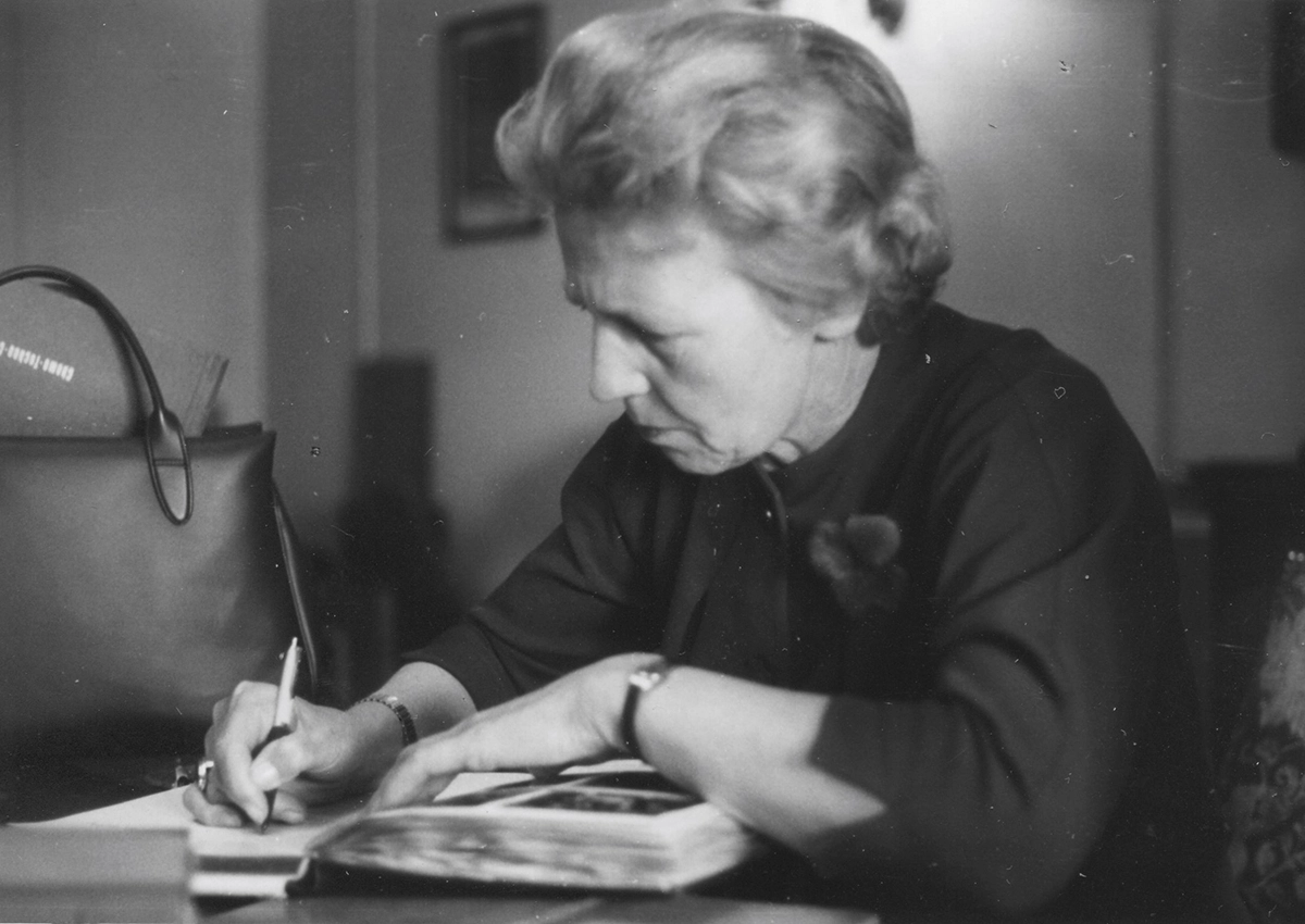 Hildegard Harlander with book and pen at her desk.